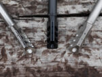 Three rifle muzzle brakes in different finishes displayed on a wooden surface.