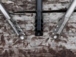 Three rifle muzzle brakes in different finishes displayed on a wooden surface.