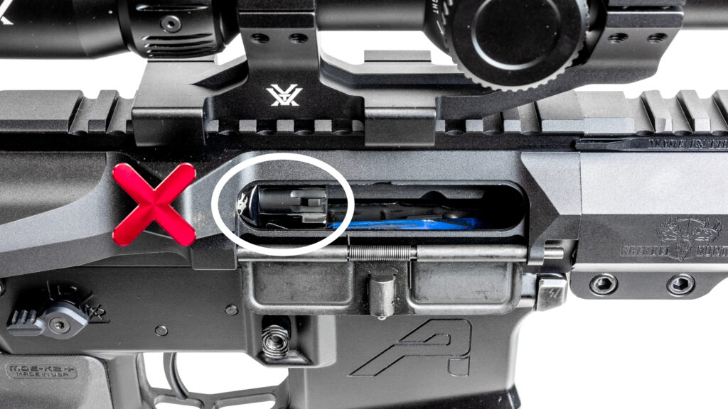 Close-up of an AR-15 ejection port with a red X, showing an incorrect bolt position where the face of the bolt carrier group is riding over top of the magazine and the front end of the bolt carrier is engaged with the bolt catch.
